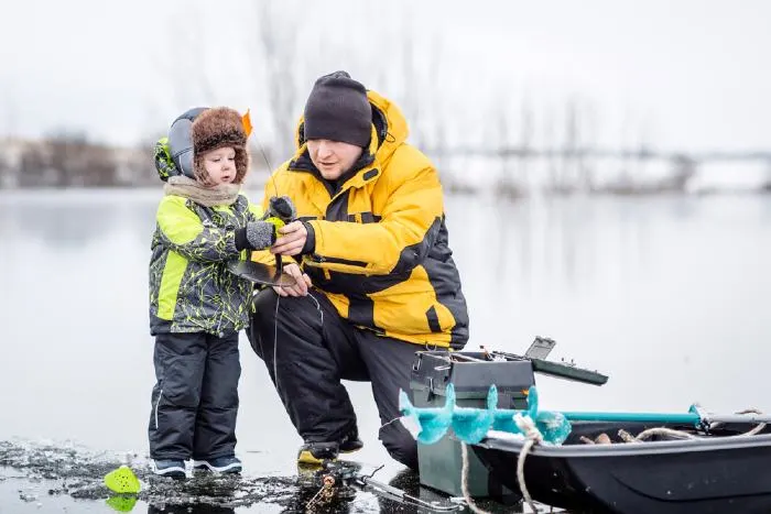Father teaching his son how to fish on a frozen lake in winter.