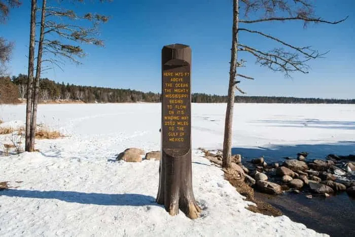 A view of an historical marker in Itasca State Park with snow on the ground. Even in winter, Itasca State Park is one of the best places to visit in Minnesota.