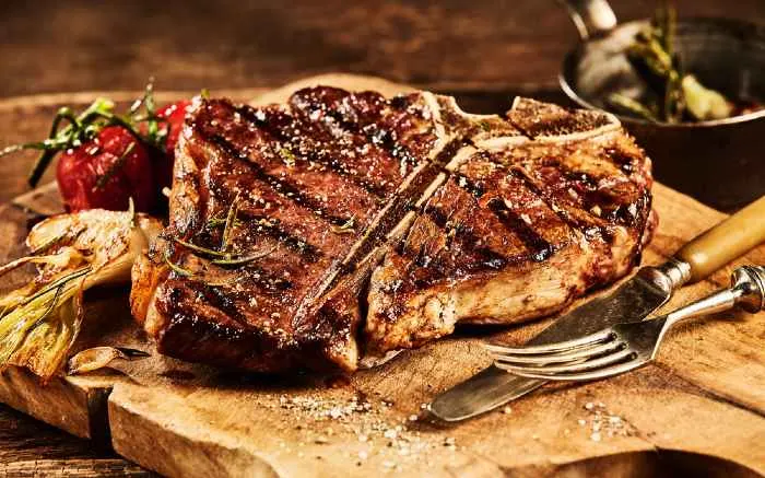 Succulent grilled large t-bone steak garnished with herbs on cutting board