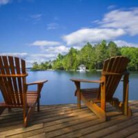 Wooden Adirondack chairs on a deck overlooking a lake