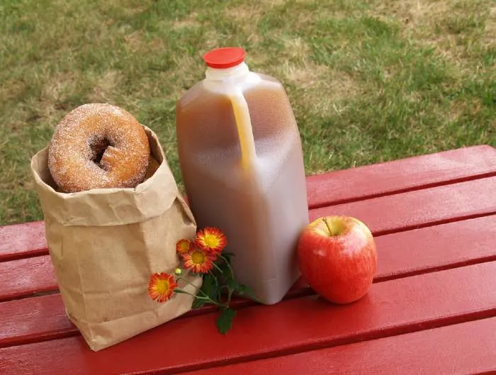 Apple cider, donuts and an apple on a red wooden table.