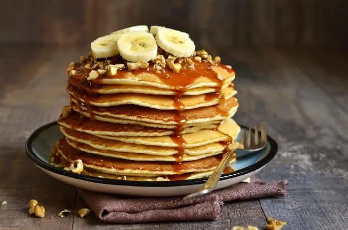 Plate served pancakes with bananas, nuts, and syrup.