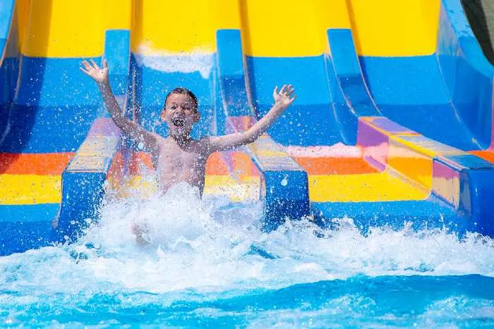 Happy cheerful boy splashing water on a water slide at one of the best indoor water parks in Minnesota