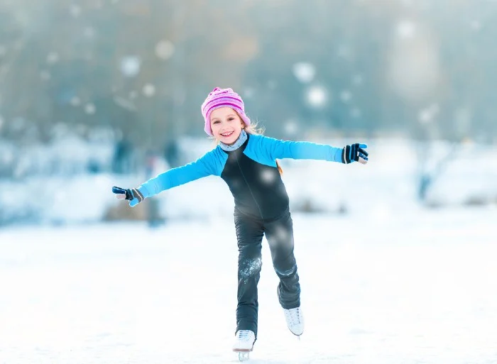 Pretty cheerful little girl in thermal suits skating outdoors
