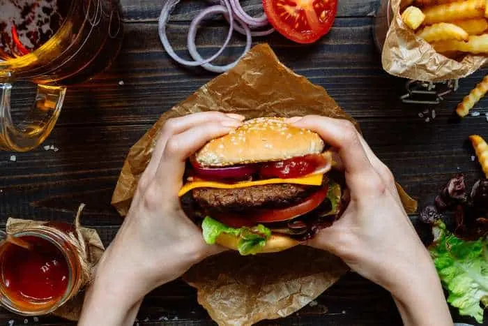 Hands holding fresh delicious burgers with french fries, sauce and beer.