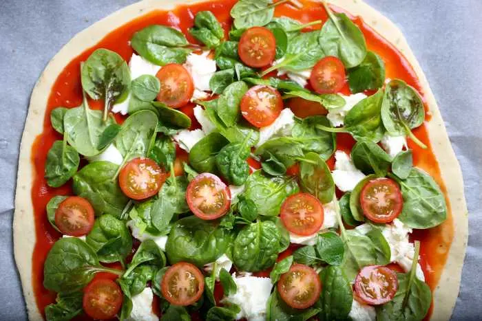 Traditional home-style pizza with spinach, tomato, and mozzarella

