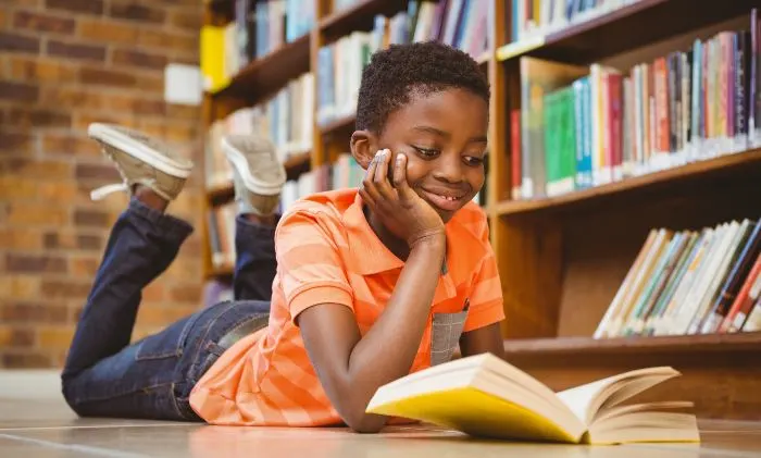 Cute african american boy reading book in library
