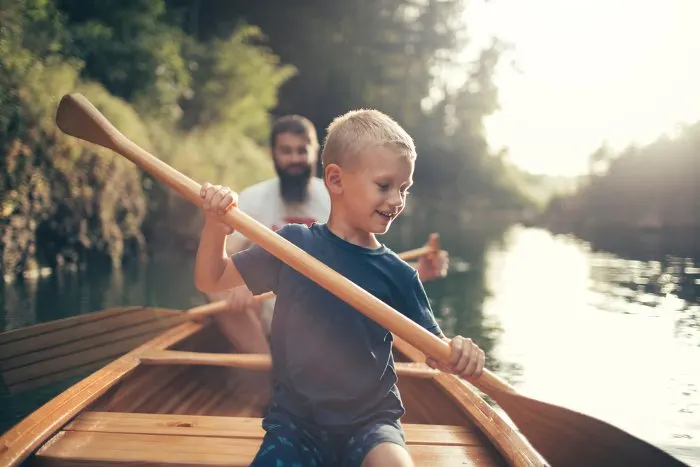 Young boy canoeing on the lake with his father
