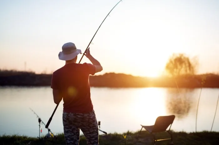 Man casting a fishing line in lake at sunset