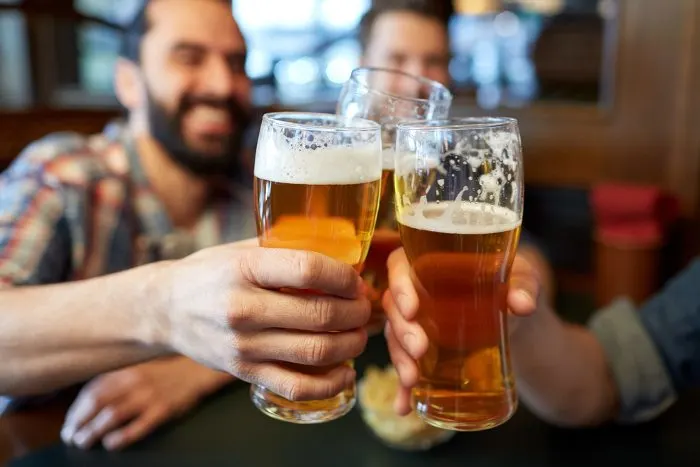 Male friends drinking beer and clinking glasses at bar