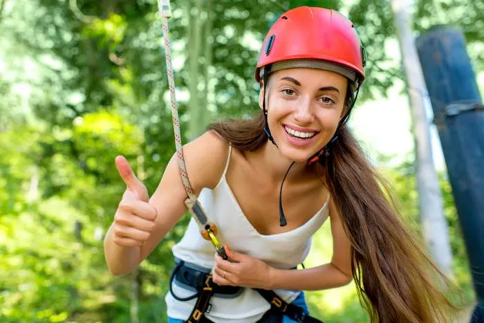 A woman in a red helmet riding on a zip line in the forest