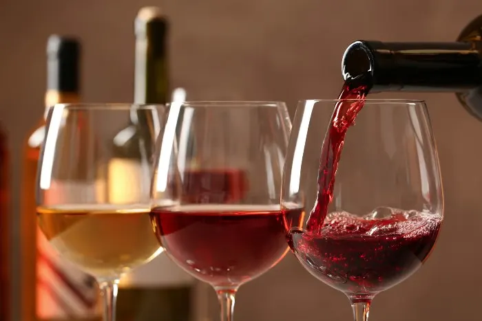Pouring wine from a bottle into glass on blurred background, closeup
