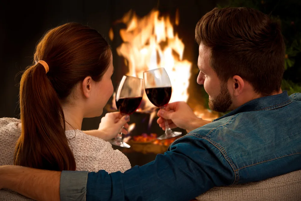 Couple relaxing with glasses of wine at romantic fireplace on winter evening