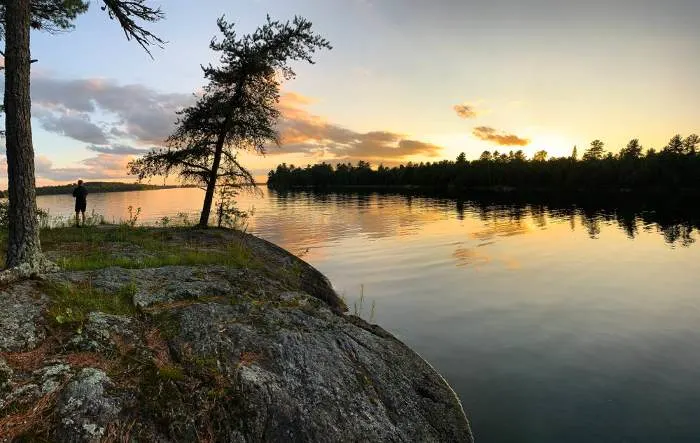 A man watches sunset from a round rock outcrop over a lake. Voyageurs National Park, Minnesota.