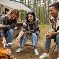 Group of young people roasting marshmallows while camping