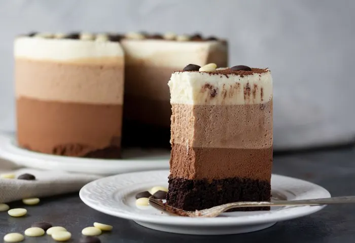 Triple chocolate mousse cake on a white plate with bite missing