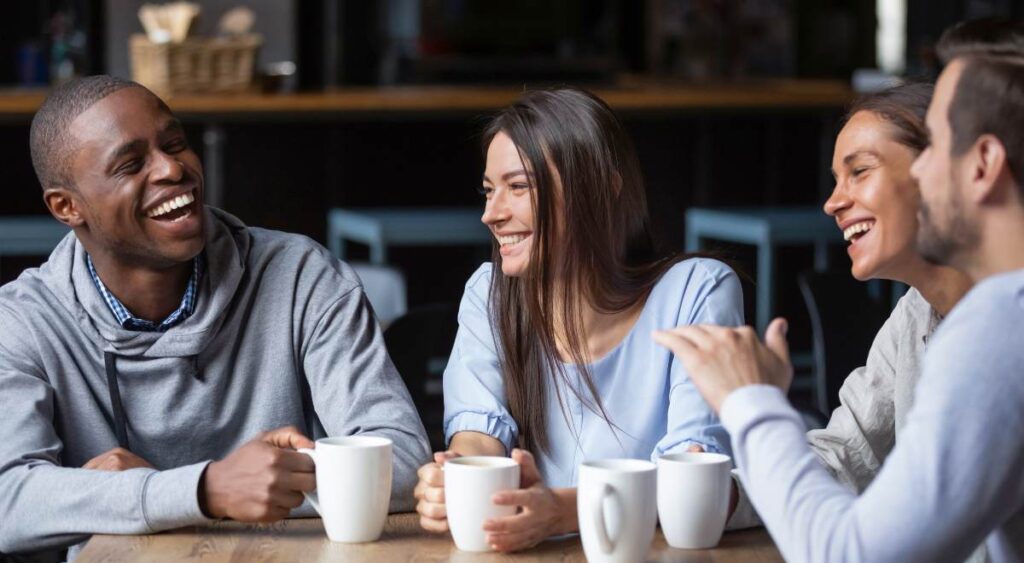 Multiracial friends girls and guys having fun laughing drinking coffee
