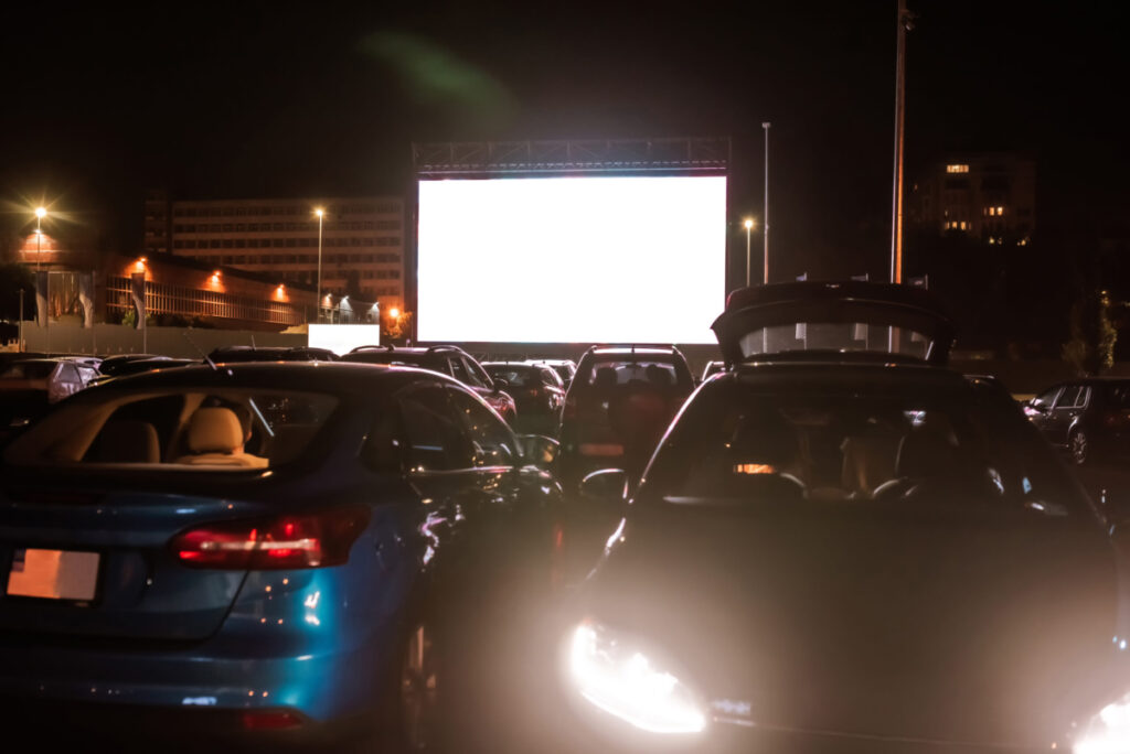 Cars at a drive in theater with a white screen.