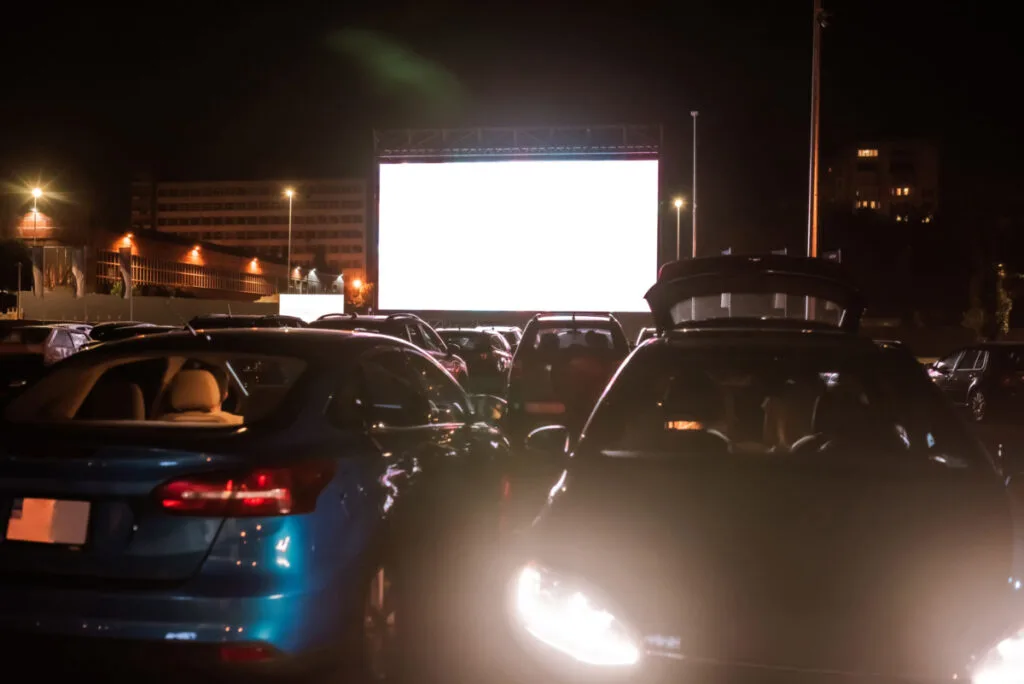 Cars at a drive in theater with a white screen.