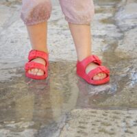 Child feet in sandals in a puddle