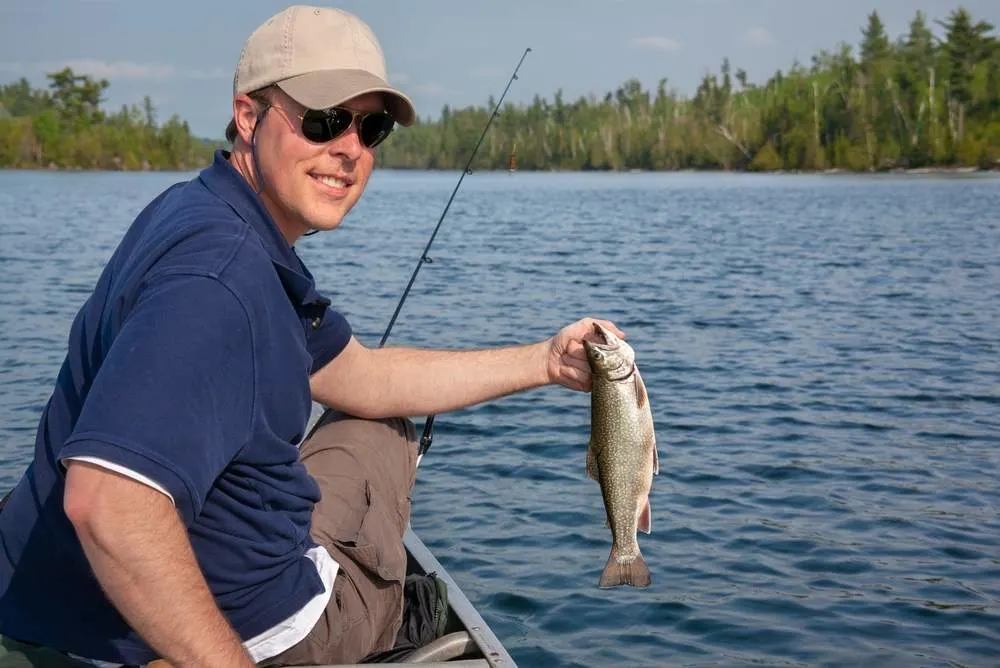 Smiling young fisherman holds up a fresh caught brook trout on northern Minnesota lake