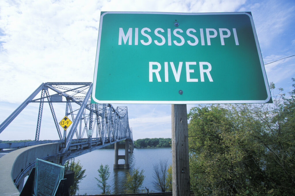 A sign that says "Mississippi River" in front of a bridge.