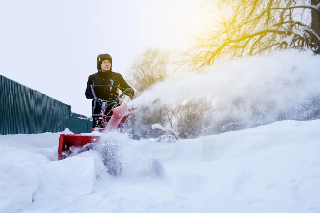 Man snow blowing with a red snow blower.