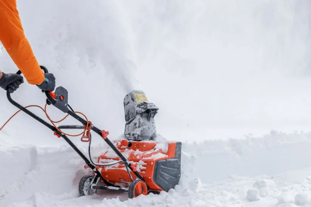 A corded snow plow pushed by an adult.