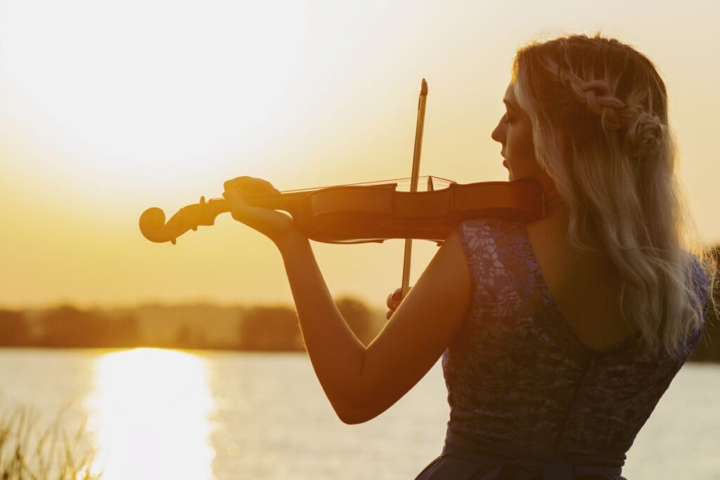 A woman playing a violin with a lake in the background.