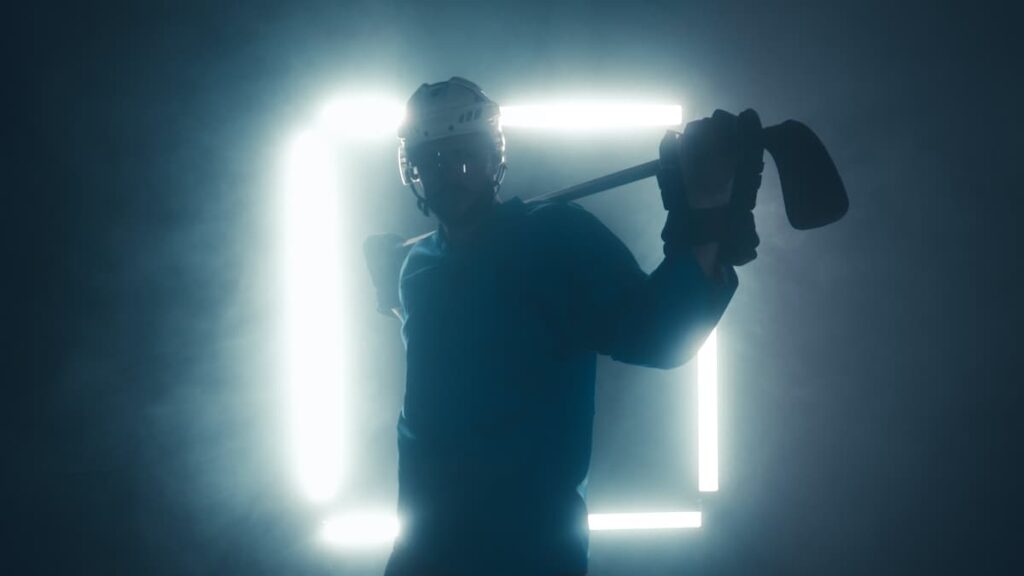 A backlit ice hockey player with stick across the shoulders.