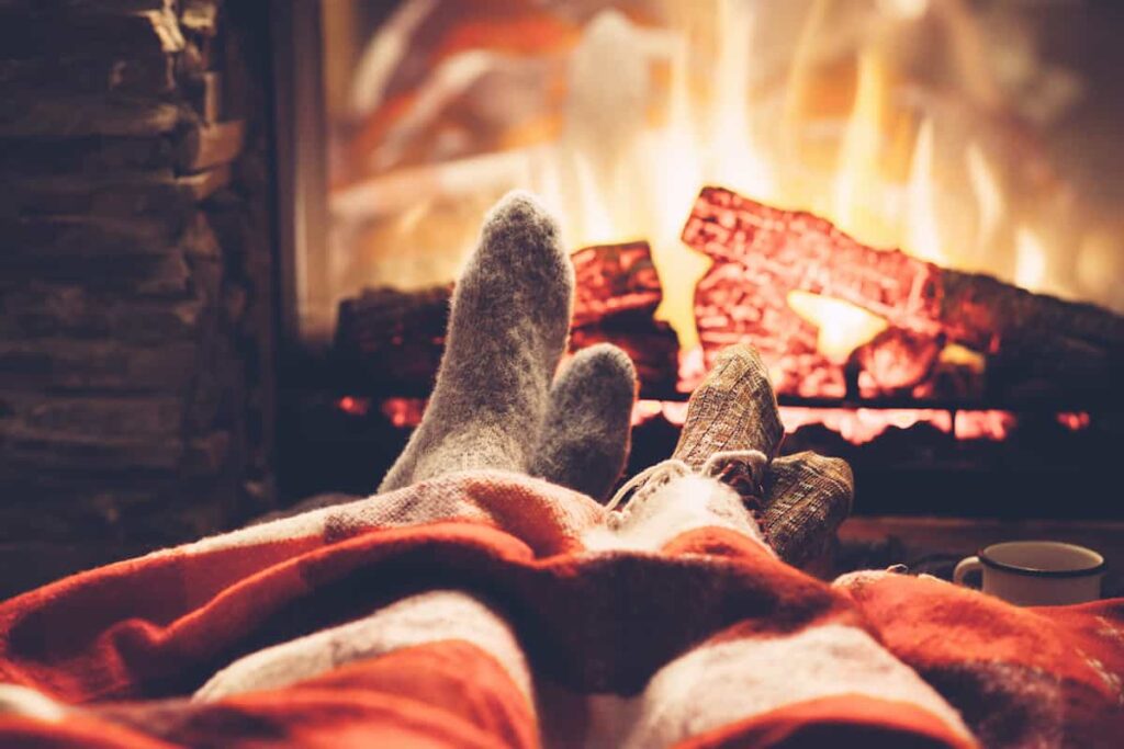 View of a couple's socked feet with a fireplace in the background.